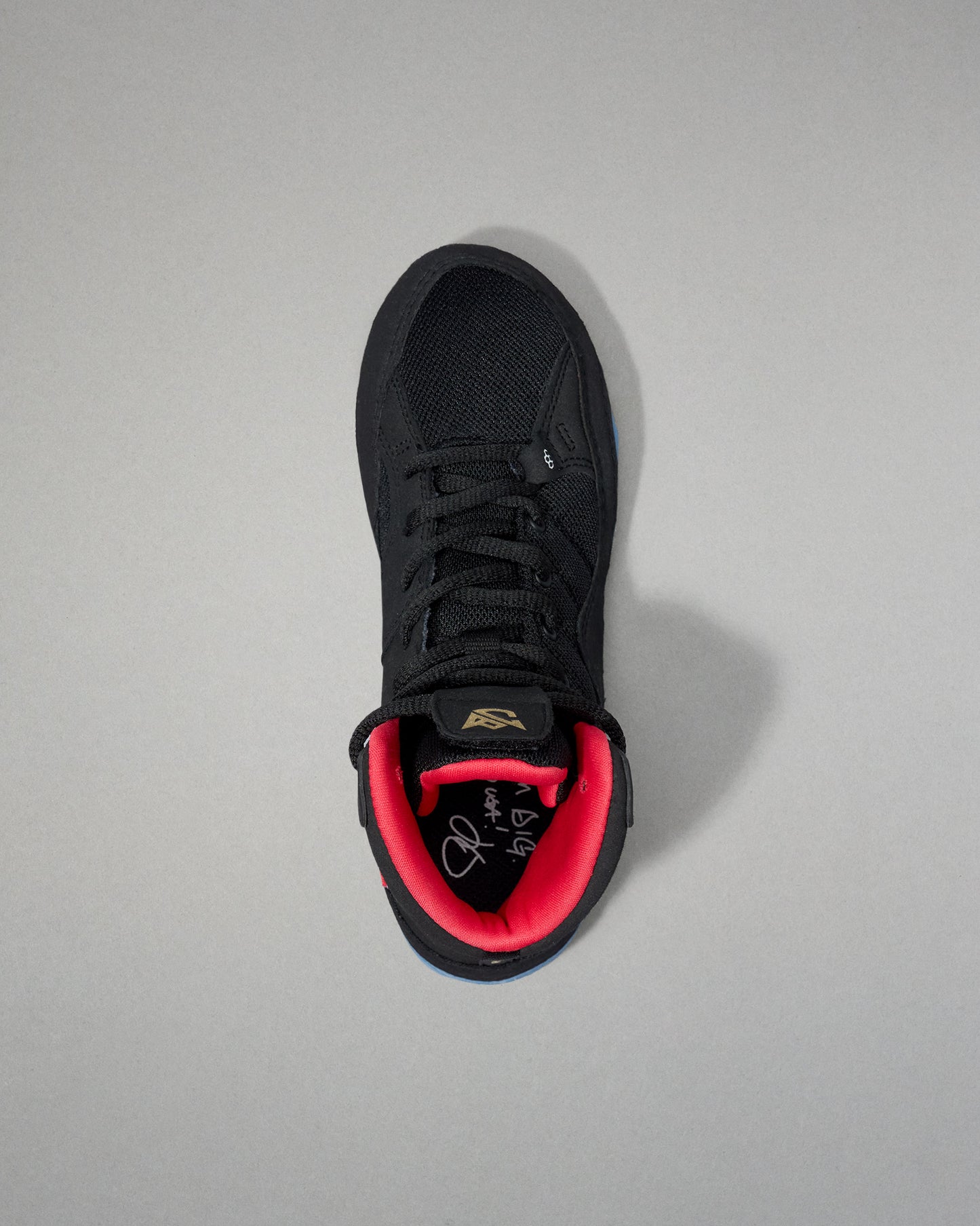 Black wrestling shoe with red lining on a gray background