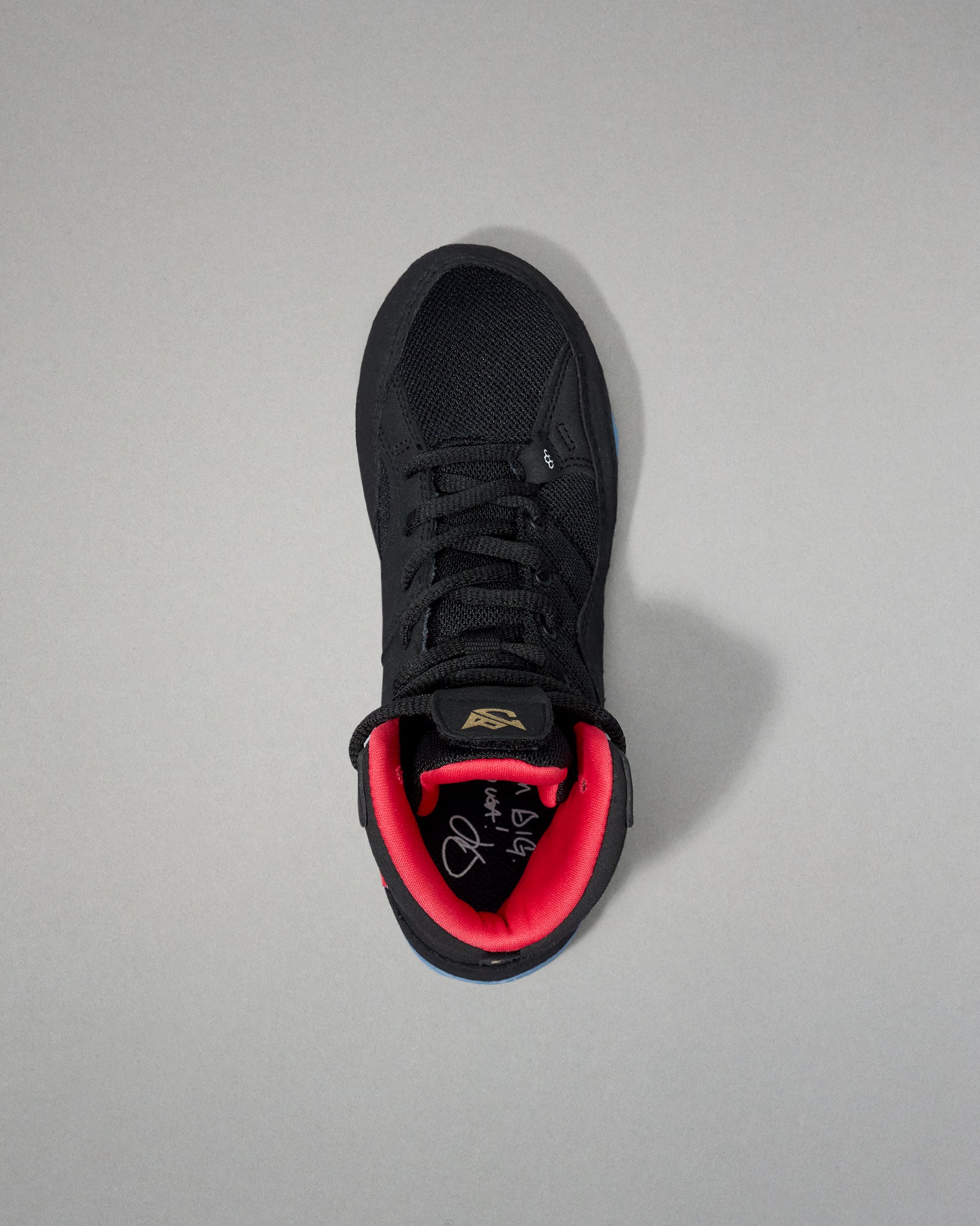 Black wrestling shoe with red lining on a gray background