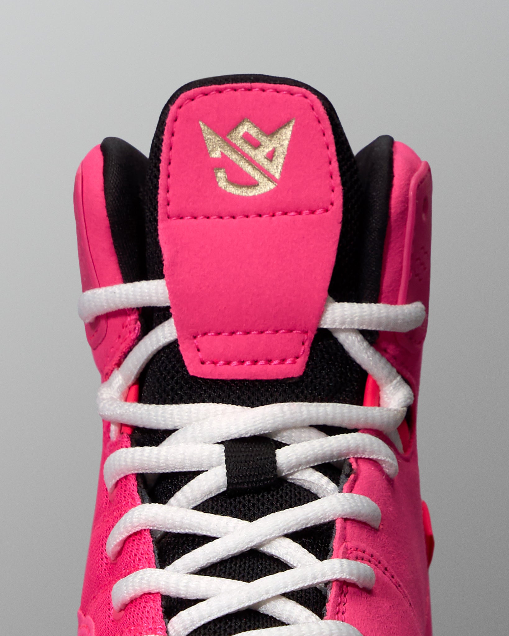 Close-up of a pink and black wrestling shoe with white laces on a gray background