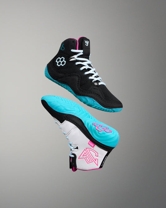 Black and turquoise wrestling shoe with pink accents on a gray background