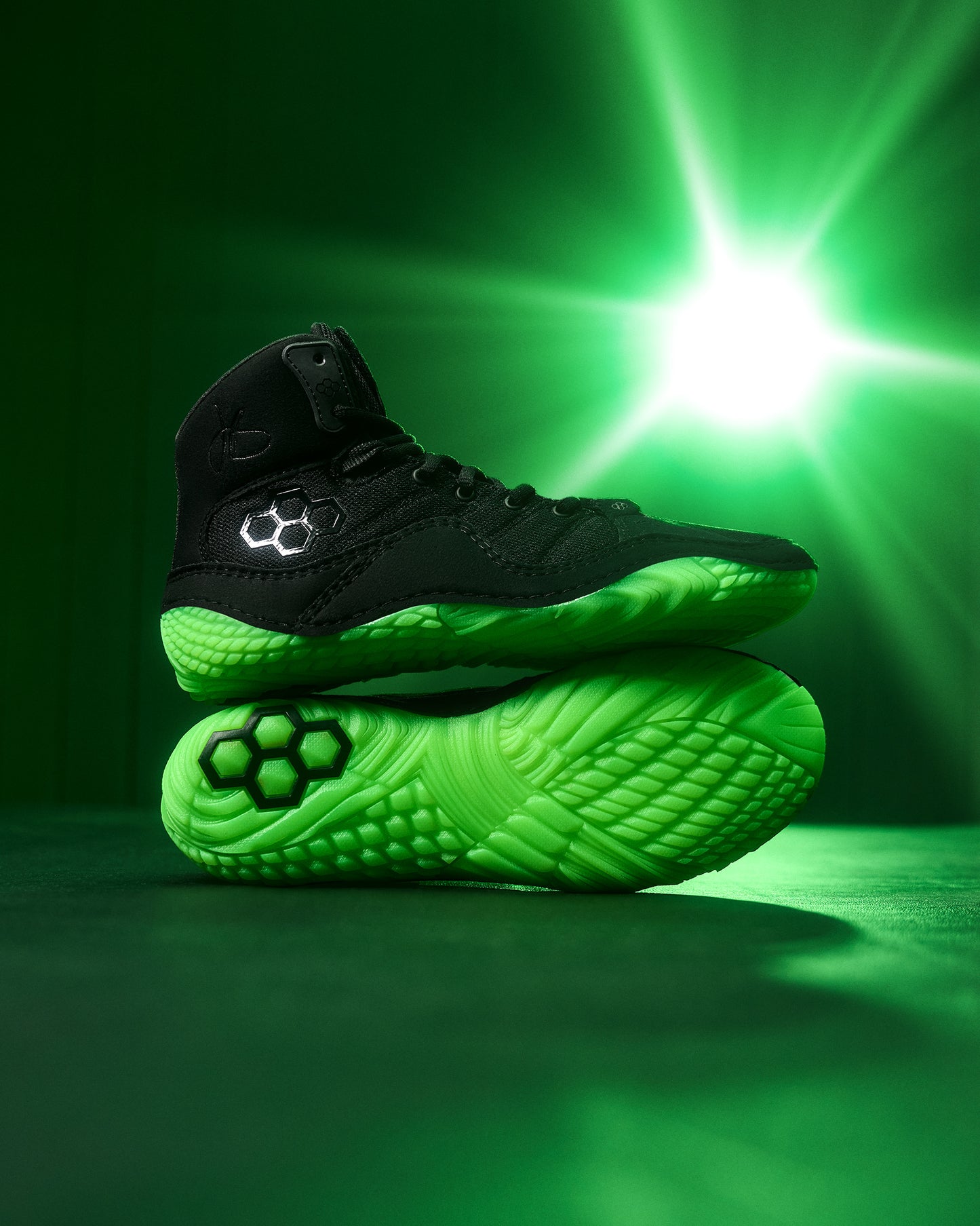 Black and green Wrestling shoes on a green background with a bright light source.