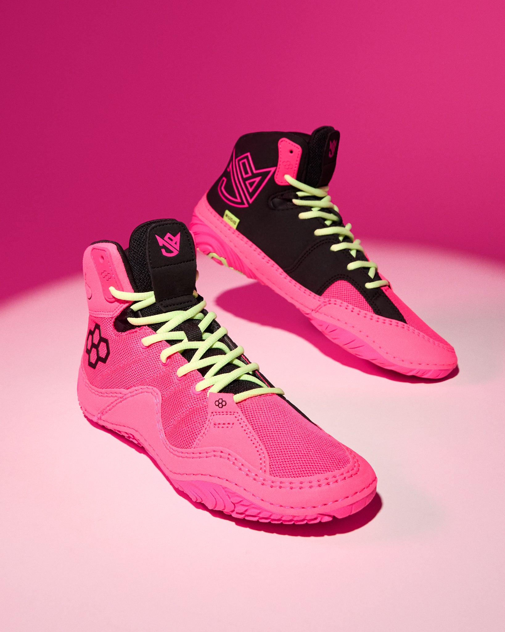 A pair of high-top wrestling shoes in vibrant neon pink and black, featuring lime green laces and a matching pink background.