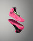 A pair of high-top athletic wrestling shoes in vibrant pink and black, shown floating against a neutral gray gradient background. One shoe is oriented to show the side profile with neon green laces, while the other shows the sole with a matching pink and black design.