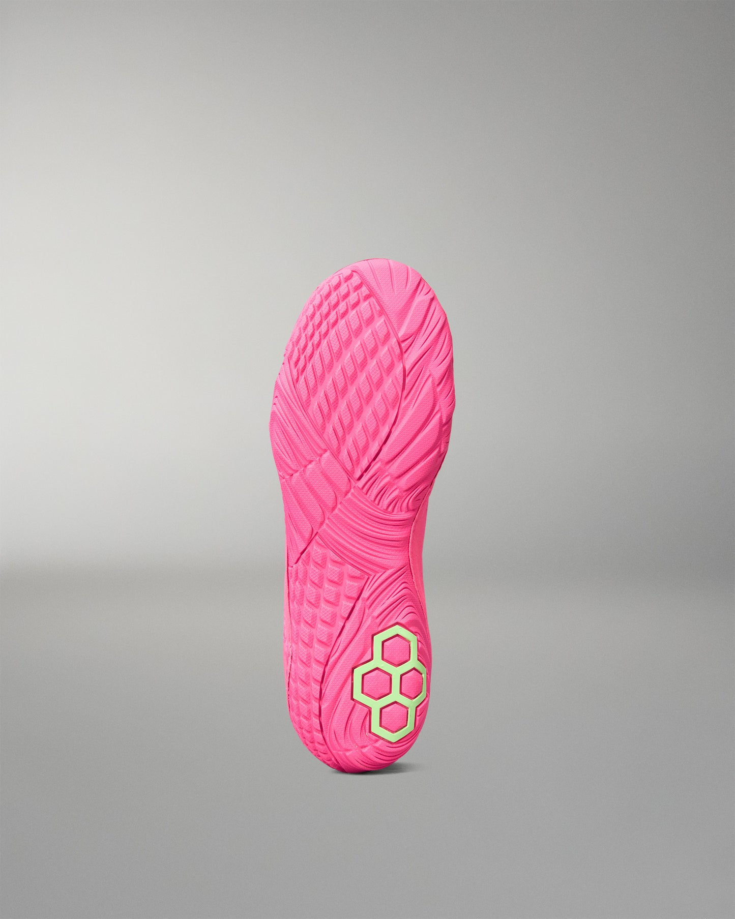 A bright pink wrestling shoe sole shown upright against a neutral gray gradient background, featuring a textured tread pattern and a small neon yellow-green geometric logo near the heel.