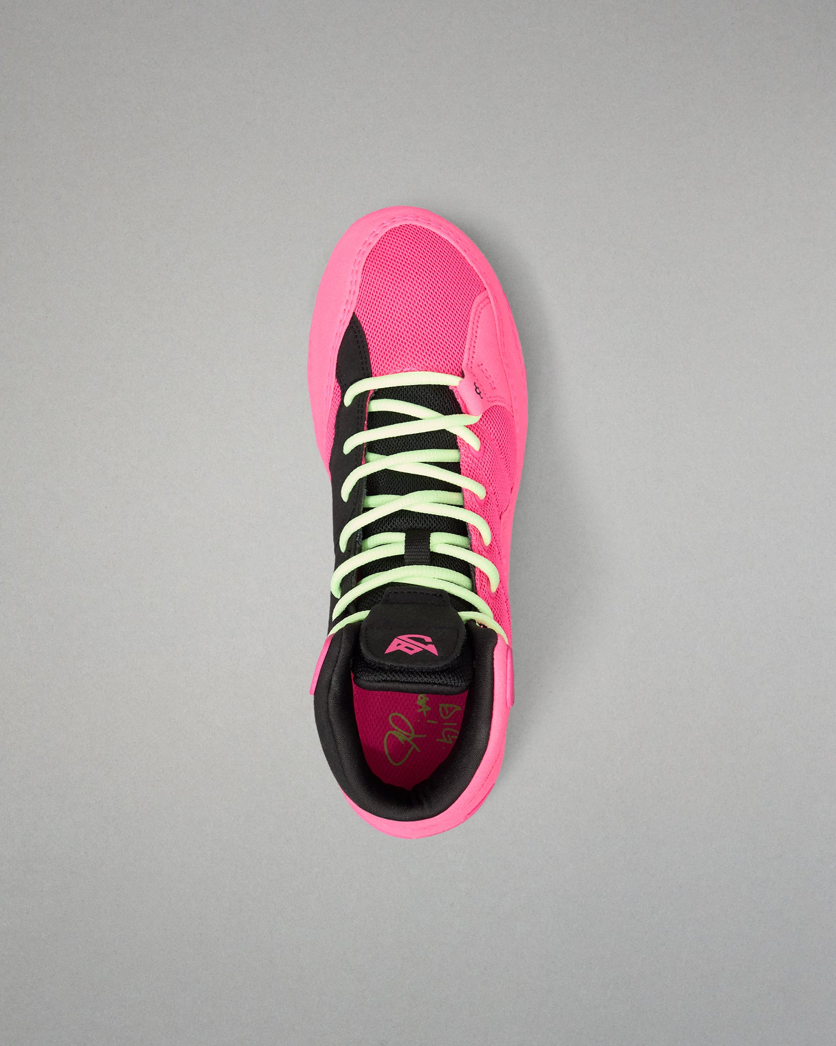 A single high-top wrestling shoe shown from a top-down view on a neutral gray background. The shoe features a vibrant hot pink upper and sole, black overlays, neon yellow-green laces, and a black collar.
