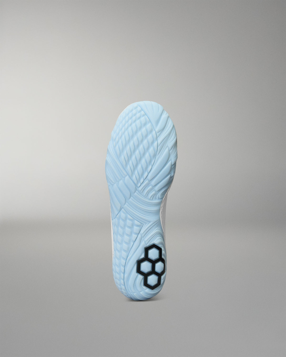 The outsole of a light blue wrestling shoe, showing a textured pattern and a black hexagonal logo near the heel, set against a neutral gray background.