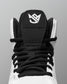 Close-up of a high-top wrestling shoe showing the black tongue patch with a white stylized logo, black laces, and white upper against a gray background.