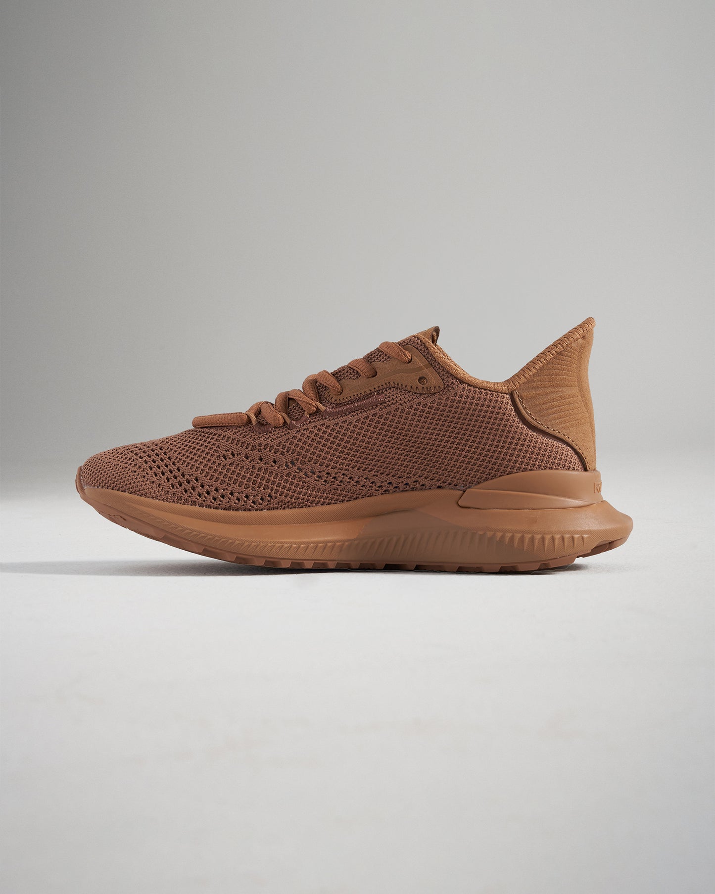 A side view of a modern brown athletic shoe featuring a breathable mesh upper and a textured sole designed for performance