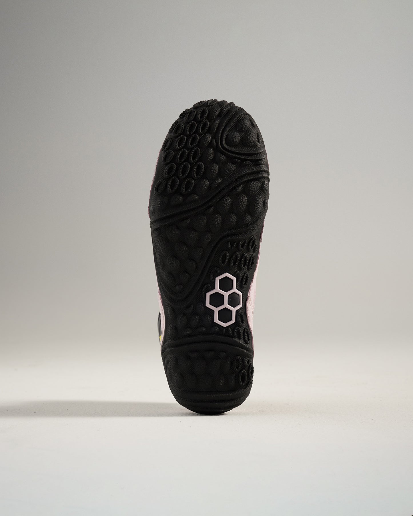 A close-up view of the textured black sole of a sneaker featuring a pink accent and a modern design