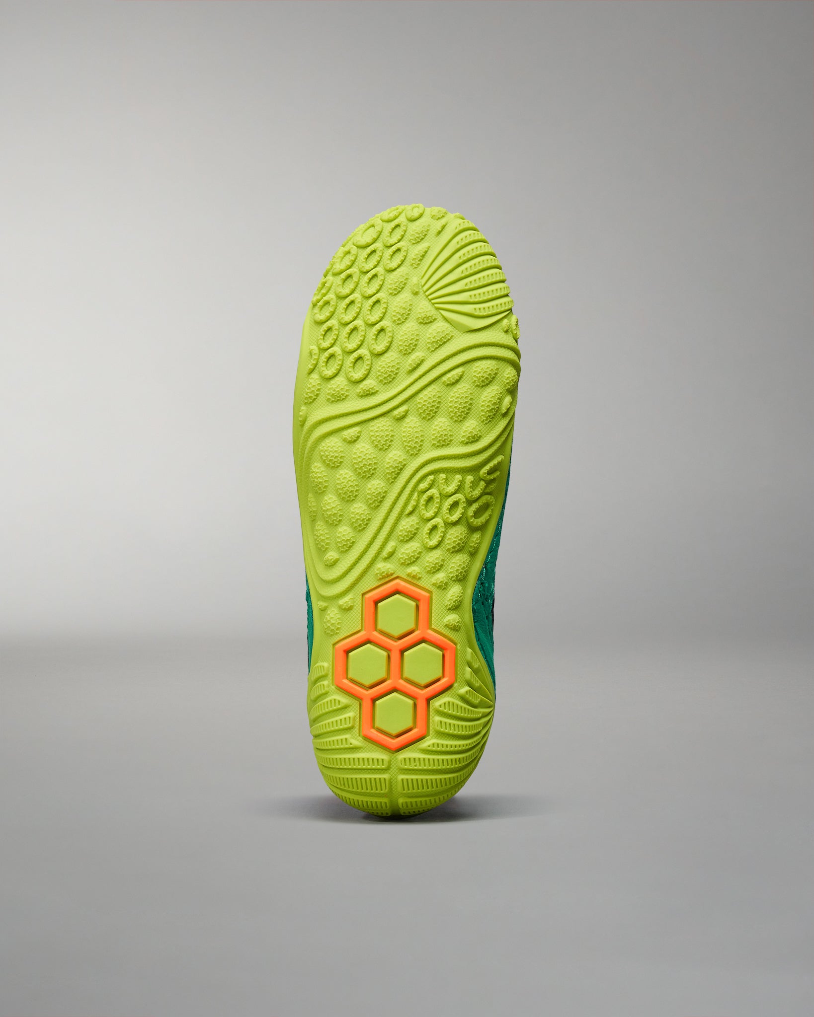 A detailed view of a vibrant green athletic shoe sole featuring a textured grip and a unique hexagonal pattern in bright orange