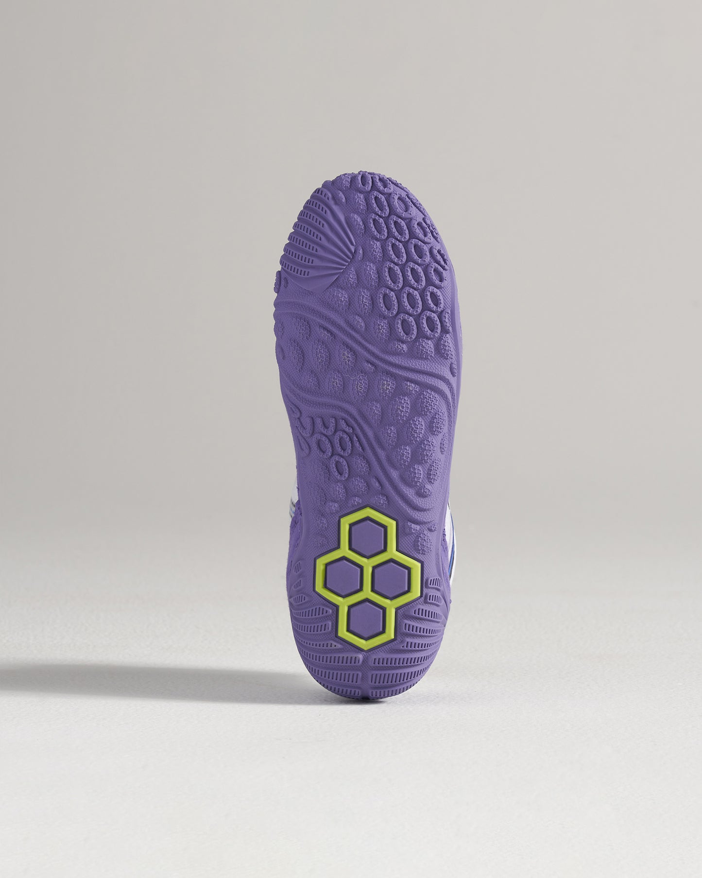 The image displays a detailed view of the sole of a purple athletic shoe featuring a unique tread pattern and a striking hexagonal logo in green