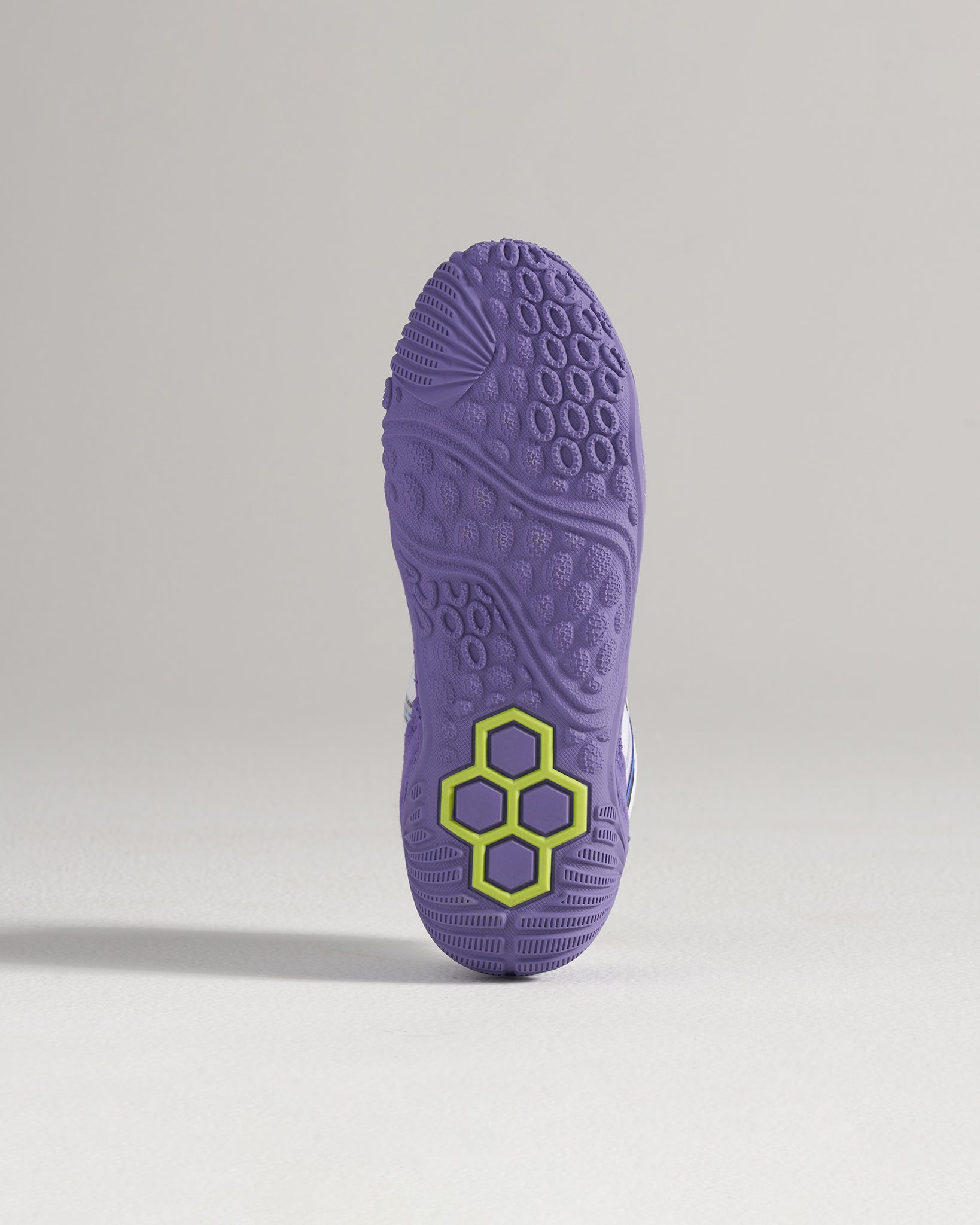 The image displays a detailed view of the sole of a purple athletic shoe featuring a unique tread pattern and a striking hexagonal logo in green