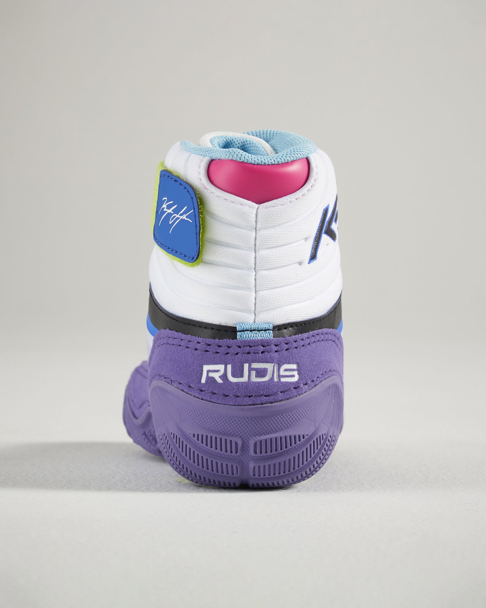 A close-up view of a stylish sneaker with a predominantly white upper featuring vibrant accents in pink blue and green and a unique textured purple sole labeled RUDIS