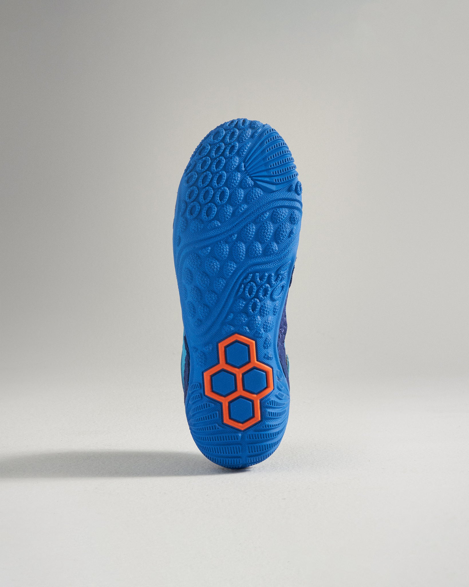 The image showcases the sole of a vibrant blue athletic shoe with an intricate textured pattern and an orange accent design