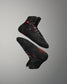 A pair of high-top black athletic shoes with red accents floats against a gray background, showcasing a sleek design and functional textured sole.