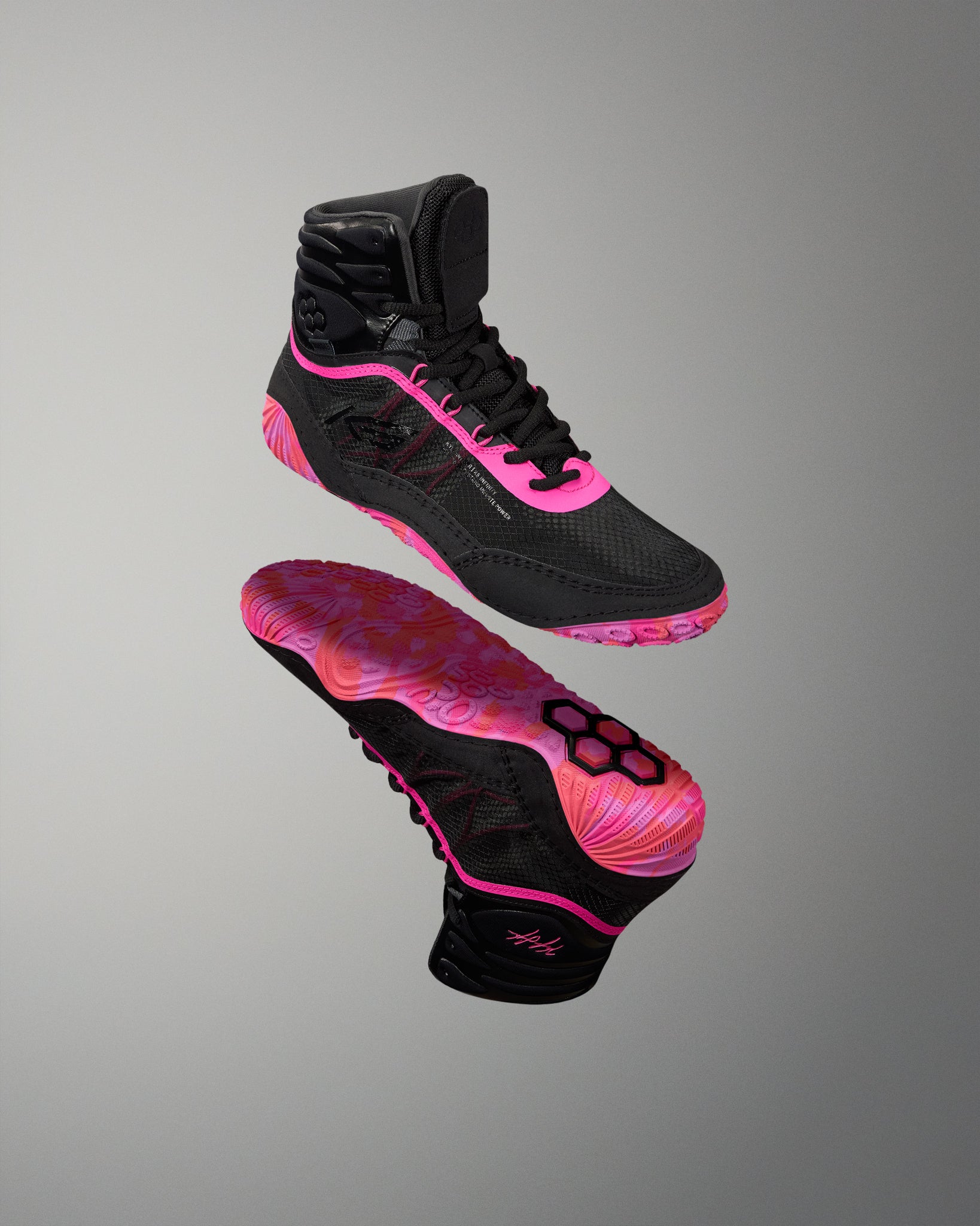 A pair of high-top athletic Wrestling shoes shown floating against a neutral gray gradient background. The shoes are primarily black with vibrant hot pink accents on the laces, side details, and outsole, featuring a distinctive pink and black patterned sole.