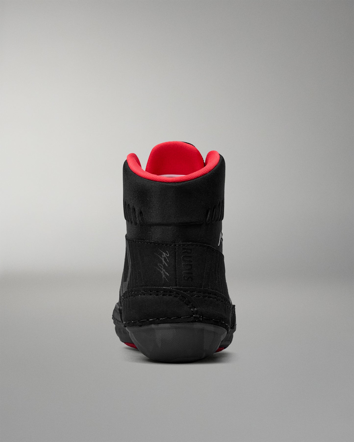 Black wrestling shoe with red lining on a gray background