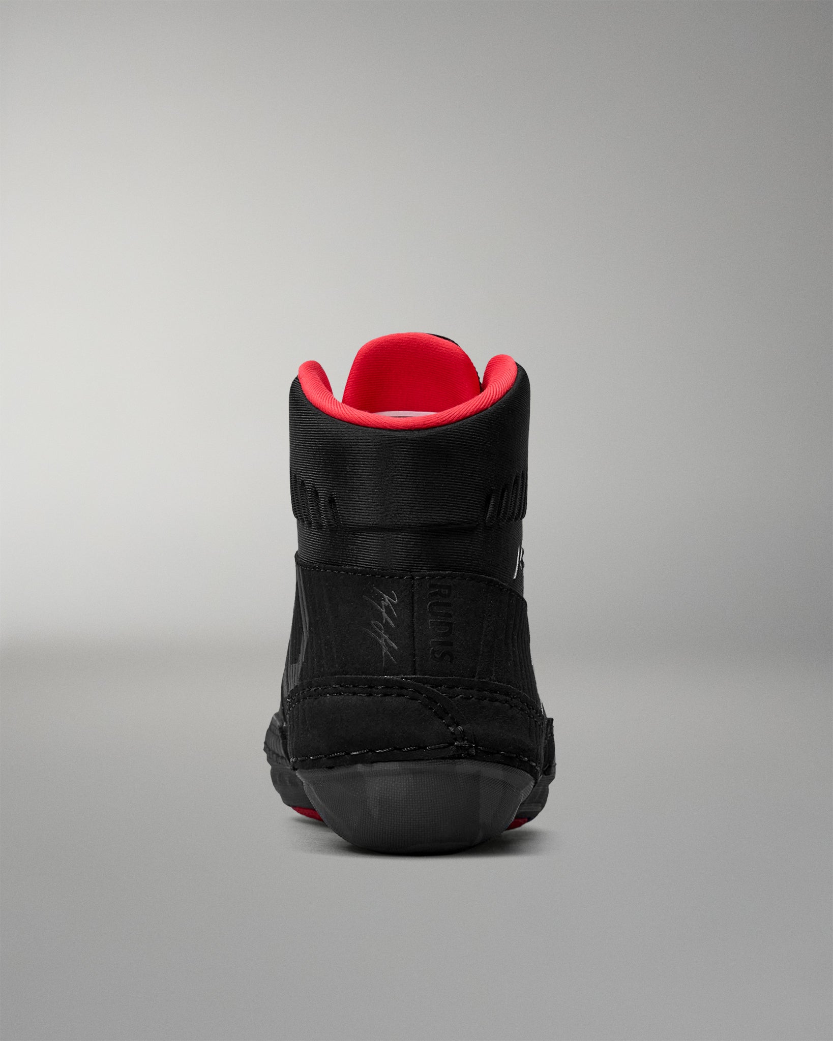 Black wrestling shoe with red lining on a gray background