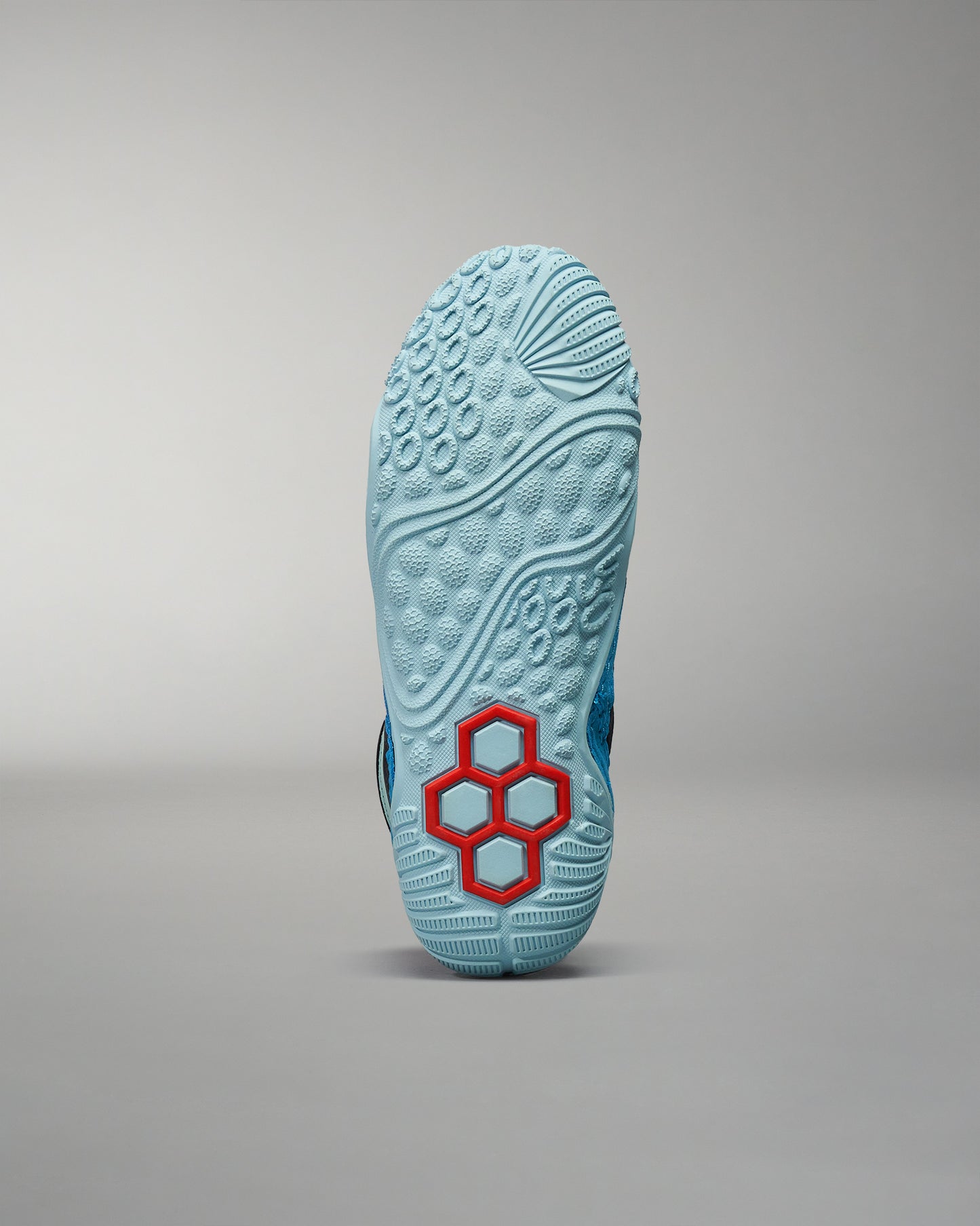 This image displays the sole of a blue athletic shoe featuring a unique red hexagonal design showcasing its textured surface for enhanced grip and performance