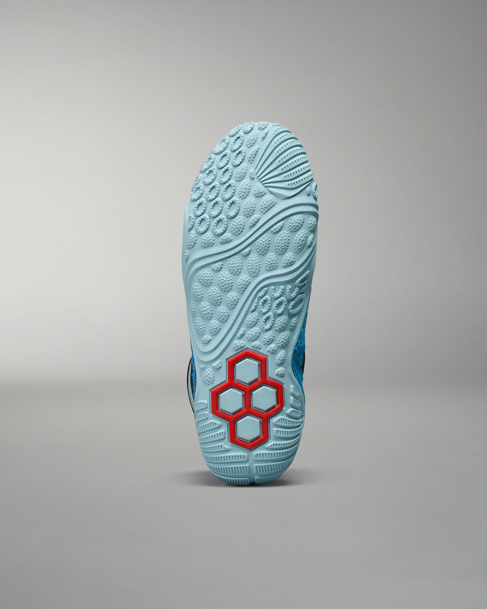 This image displays the sole of a blue athletic shoe featuring a unique red hexagonal design showcasing its textured surface for enhanced grip and performance
