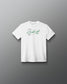 A white short-sleeve crewneck t-shirt with a green signature-style graphic and small text on the chest, displayed against a dark gray gradient background.