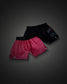 Two pairs of athletic fight shorts displayed against a dark gray gradient background. The pair in the foreground is bright pink with a black waistband featuring the brand name 'RUDIS' in white.