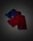 Two pairs of athletic boxing shorts, one red and one blue, displayed in a layered flat-lay arrangement on a dark gray gradient background.