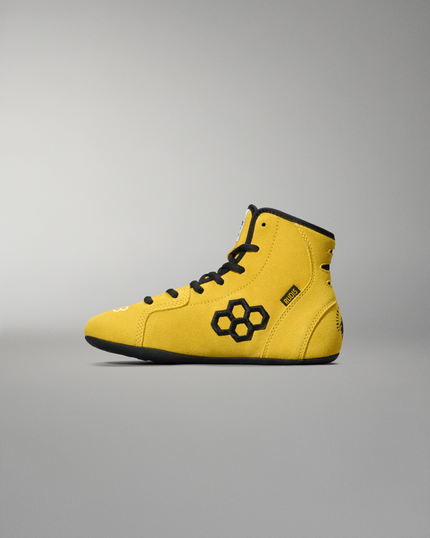 Yellow wrestling shoes with black RUDIS Hex Logo accents on a gray background