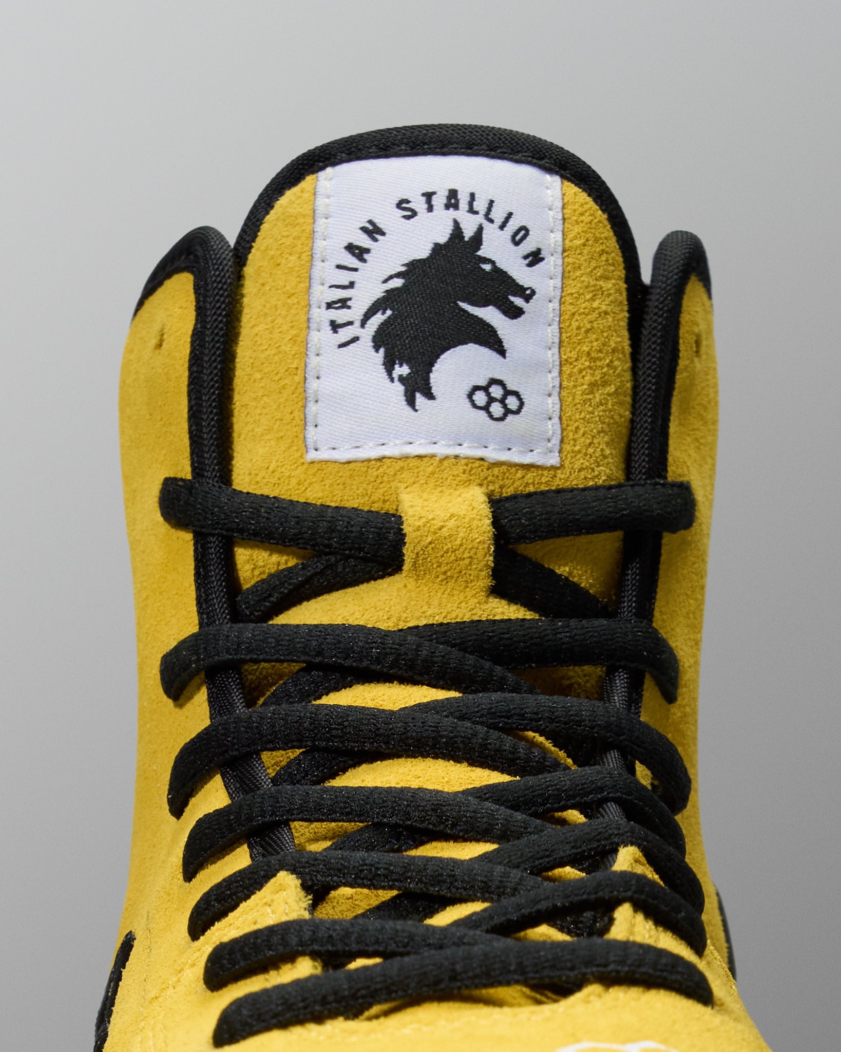 Yellow wrestling shoes with black laces and 'Italian Stallion' logo on a gray background