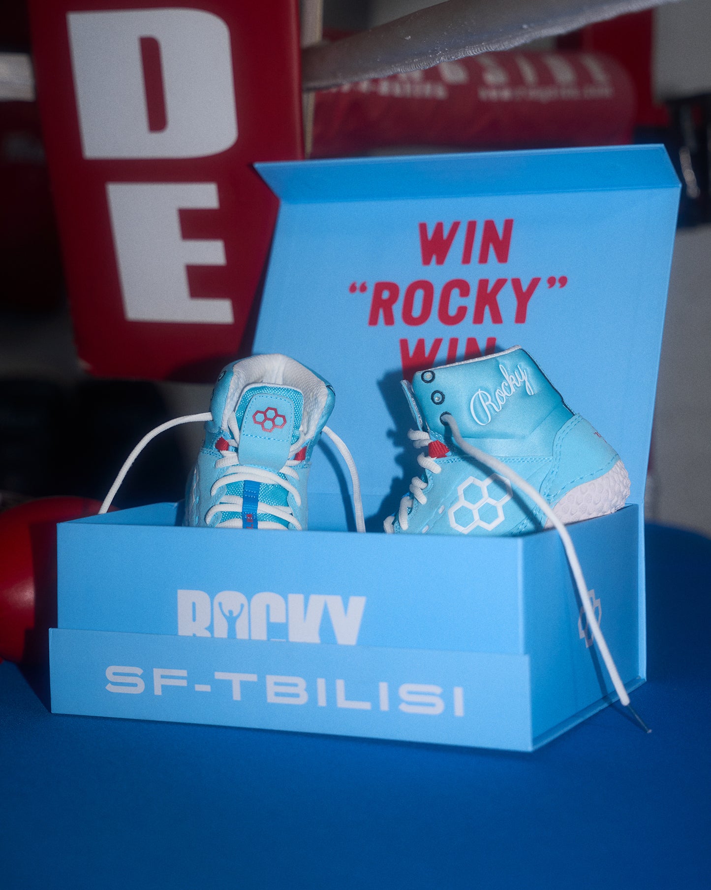 Blue shoe box with wrestling shoes and 'Rocky' branding, featuring a promotional message.