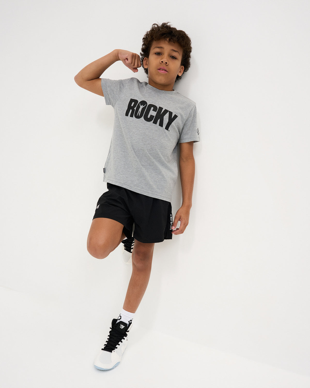 RUDIS Rocky Brand Youth T-Shirt in Gray, featuring the signature black ROCKY chest graphic and RUDIS sleeve logo in a full-length athletic lifestyle look.