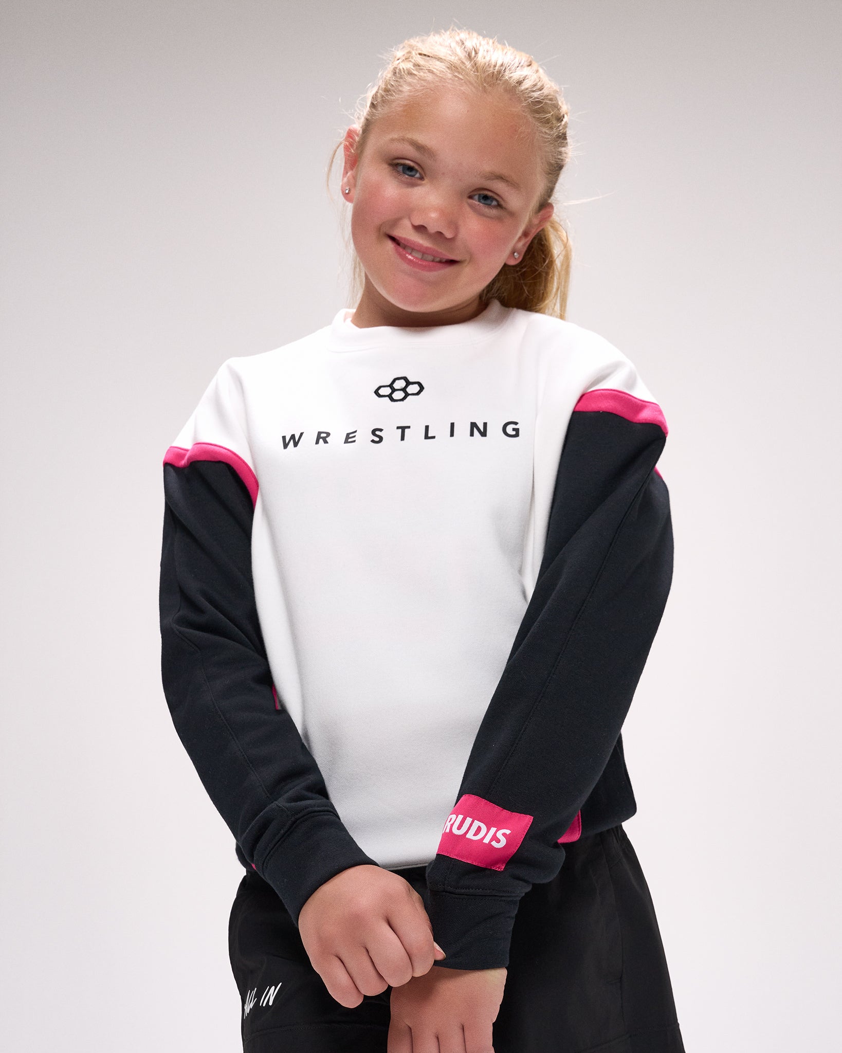 Young girl wearing a wrestling-themed sweatshirt with visible branding on a plain background