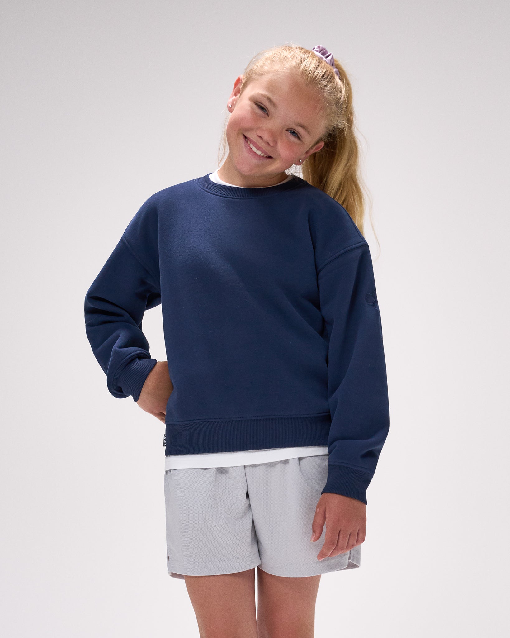 Young girl wearing a navy blue sweatshirt and light gray shorts on a white background