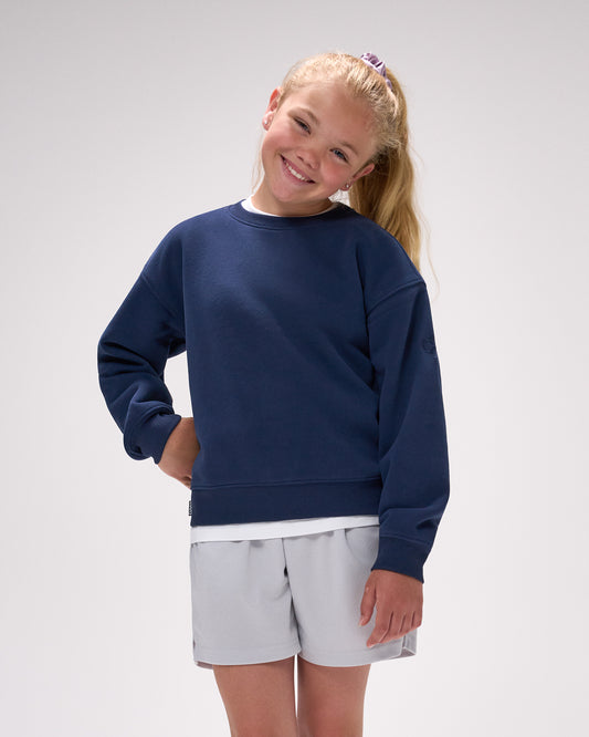 Young girl wearing a navy blue sweatshirt and light gray shorts on a white background
