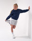Young girl in navy sweater and gray shorts stretching against a white background