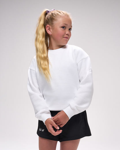 Young girl wearing a white crewneck and black skirt on a plain background