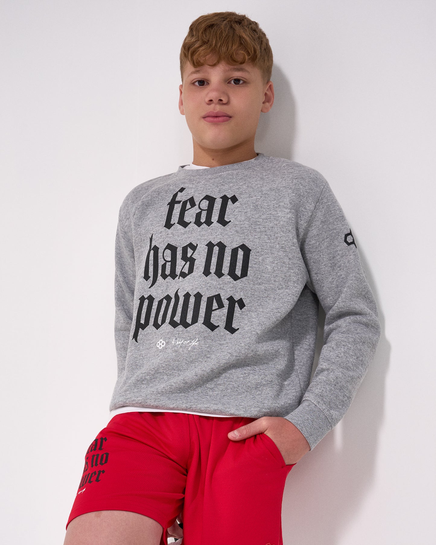 Person wearing a gray sweatshirt with 'fear has no power' text and red shorts on a white background