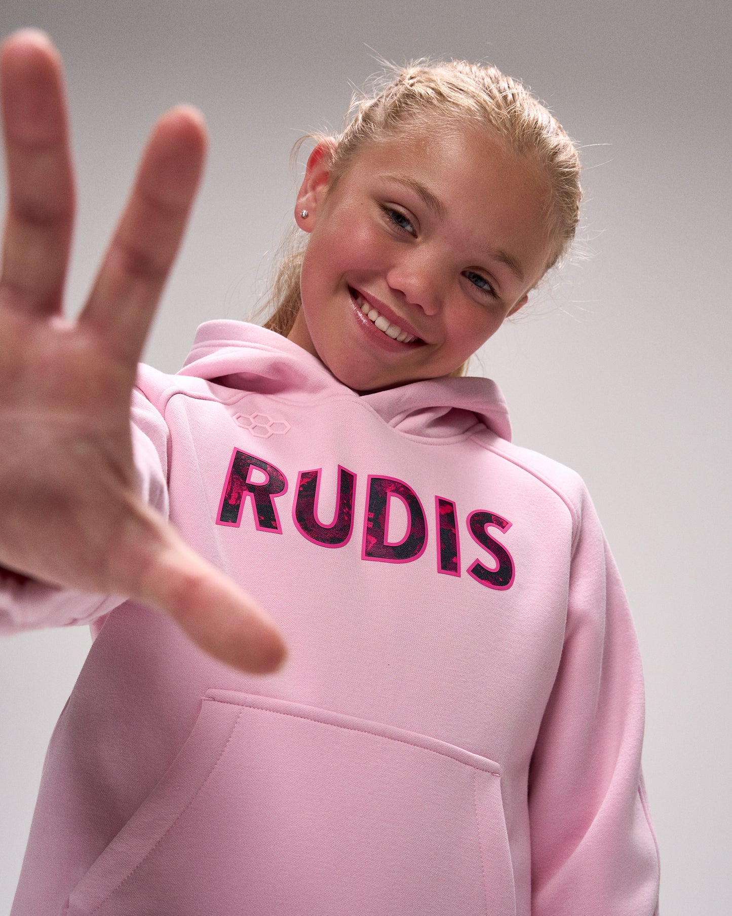 Person wearing a pink hoodie with 'RUDIS' branding, making a peace sign.