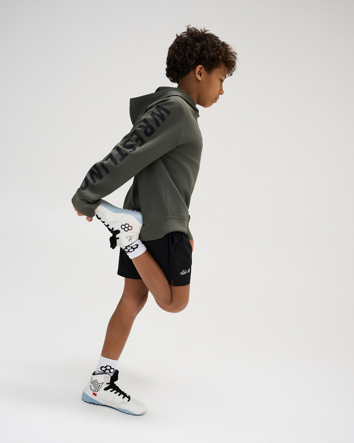 Side profile of the RUDIS Wrestling Youth COOL FEEL Hoodie in Dark Olive, highlighting the hood, athletic silhouette, and oversized black WRESTLING sleeve graphic.