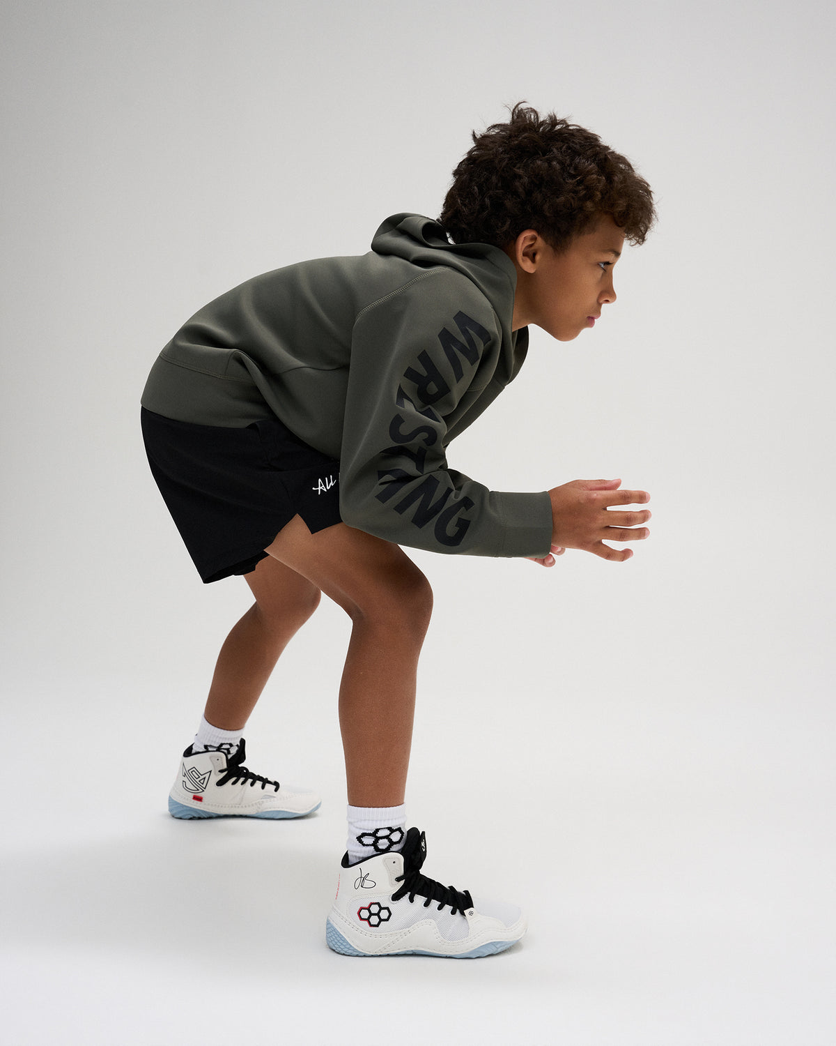 RUDIS Wrestling Youth COOL FEEL Hoodie in Dark Olive shown in an athletic wrestling stance, showcasing flexible movement and bold sleeve branding.