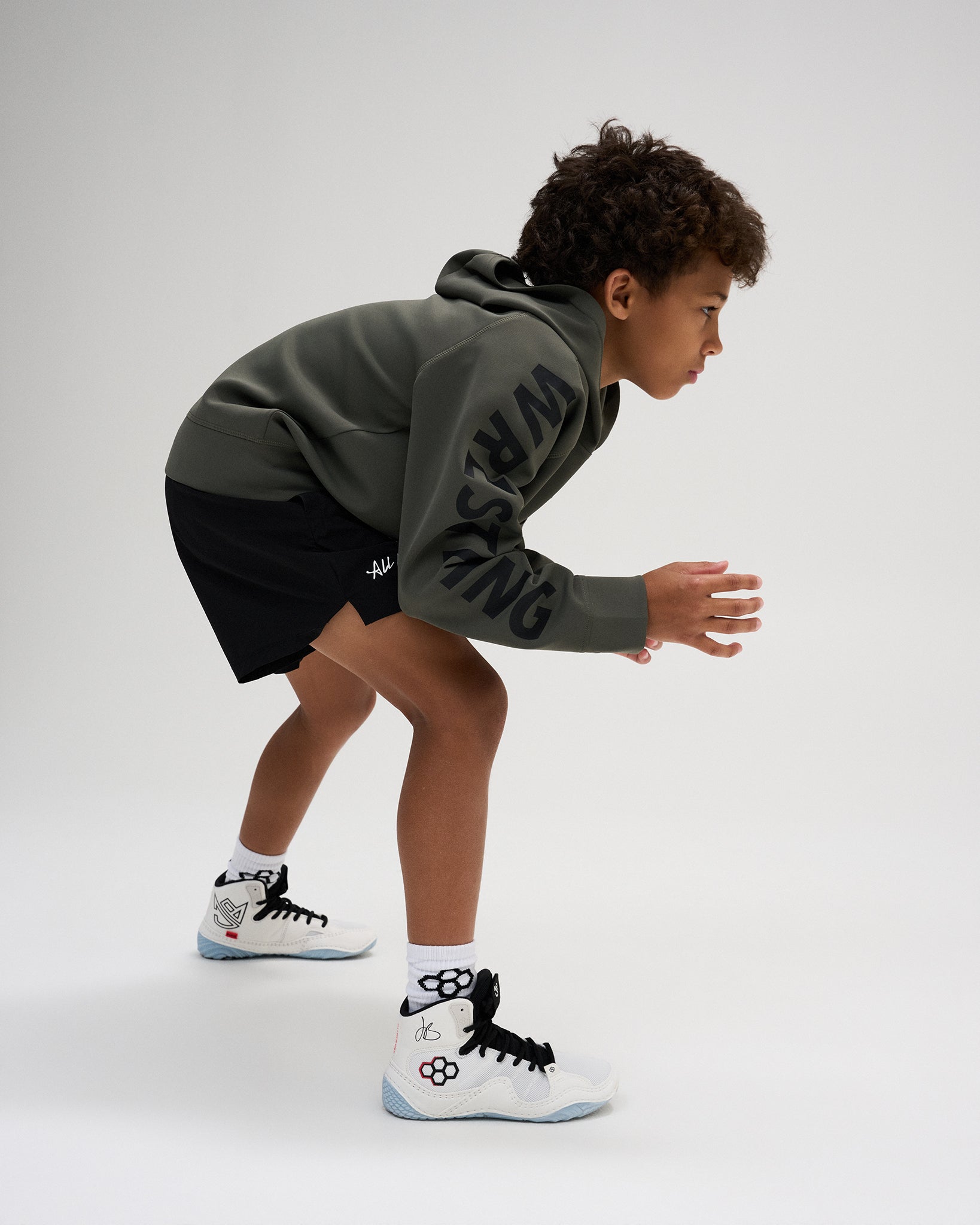 RUDIS Wrestling Youth COOL FEEL Hoodie in Dark Olive shown in an athletic wrestling stance, showcasing flexible movement and bold sleeve branding.