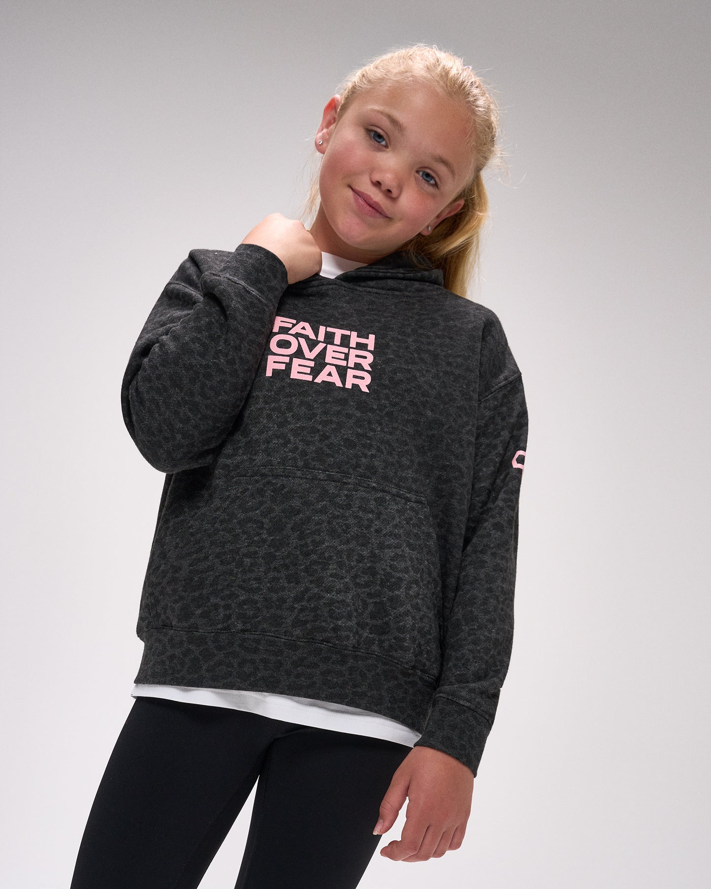 Young girl wearing a dark gray hoodie with 'Faith Over Fear' text on a plain background