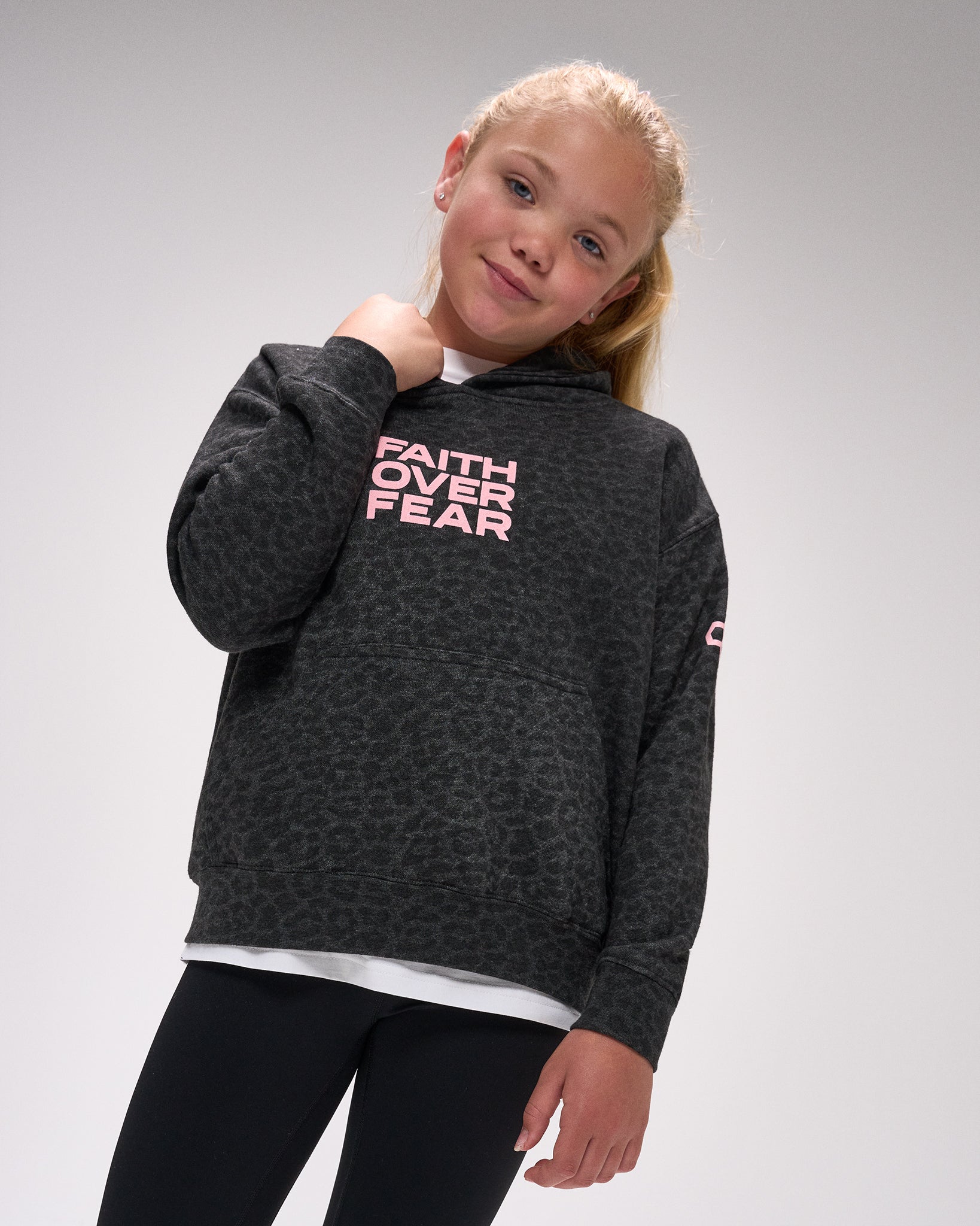 Young girl wearing a dark gray hoodie with 'Faith Over Fear' text on a plain background