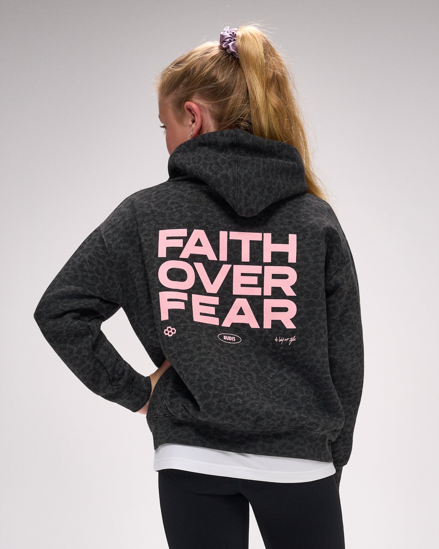Person wearing a dark hoodie with 'Faith Over Fear' text on the back against a gray background