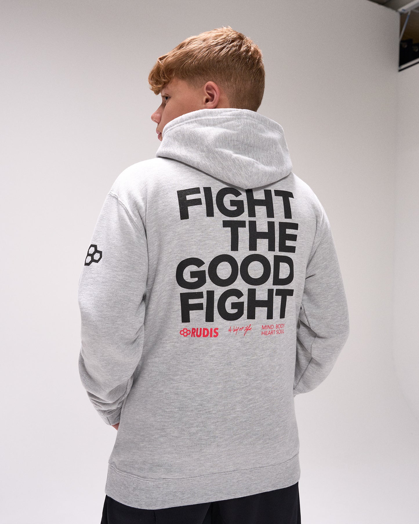Person wearing a gray hoodie with 'Fight the Good Fight' text on the back, standing against a plain background.