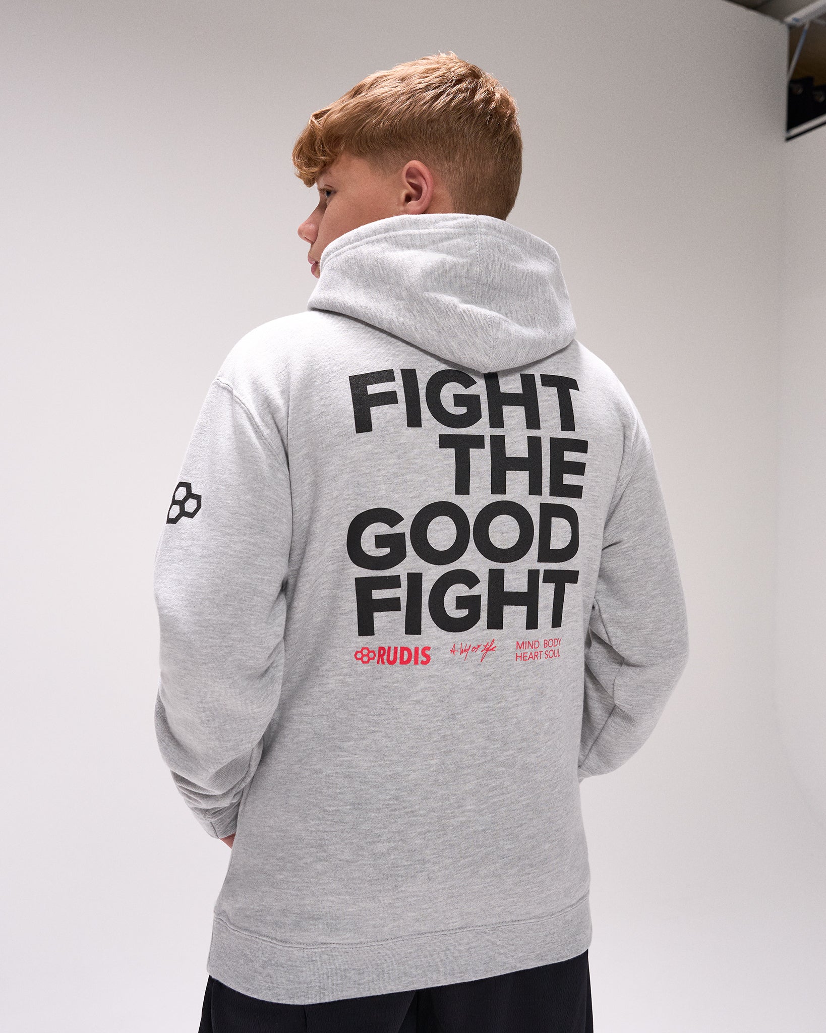 Person wearing a gray hoodie with 'Fight the Good Fight' text on the back, standing against a plain background.