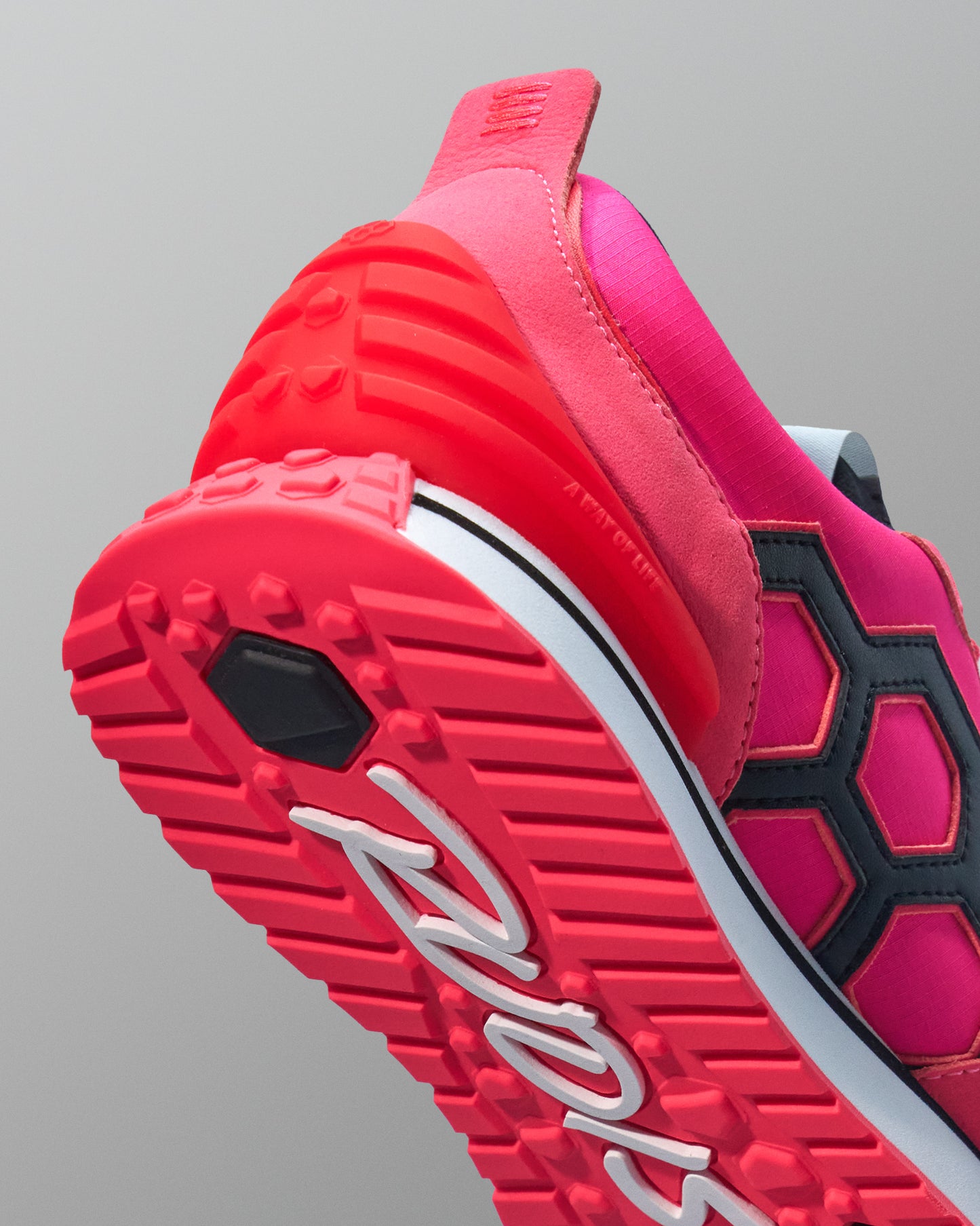 Close-up of a pink and red running shoe with a textured sole on a gray background