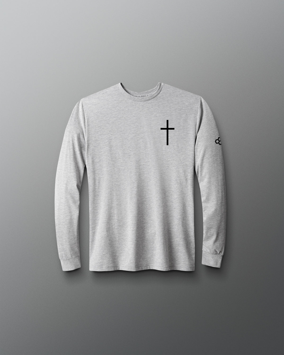 A light gray long-sleeve crewneck shirt with a black cross printed on the left chest and a small black logo on the right sleeve, displayed against a dark gray gradient background.