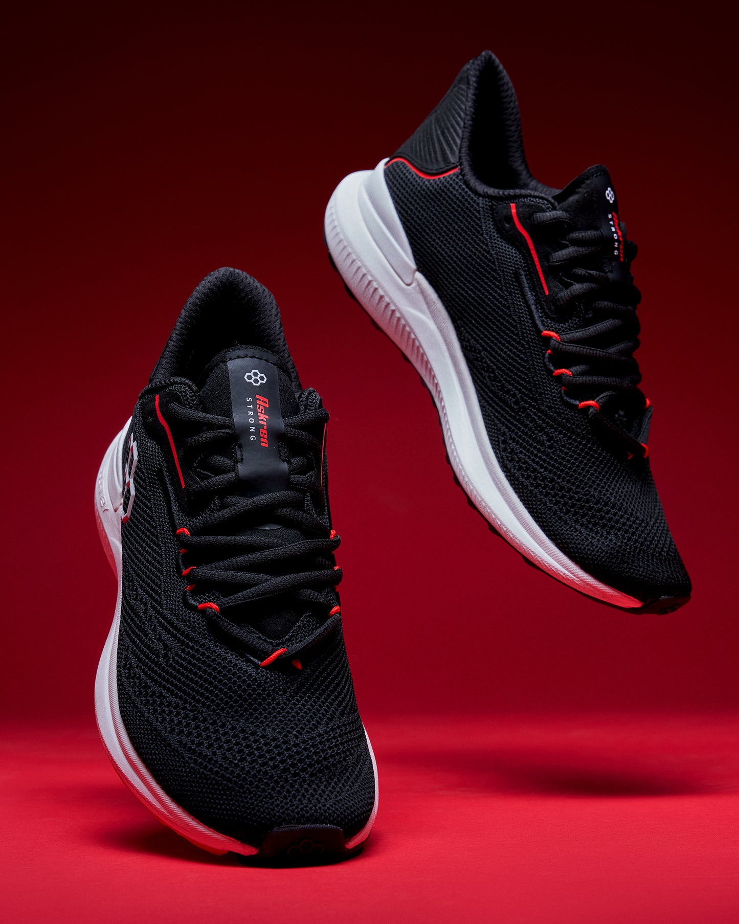 Black running shoes with red accents on a red background