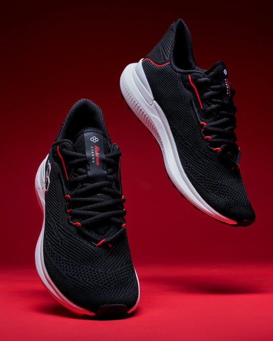 Black running shoes with red accents on a red background
